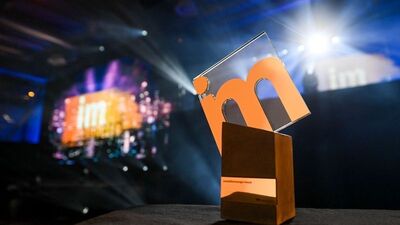 Der IMA-Award steht im Vordergrund, im Hintergrund ist die Bühne der Preisverleihung mit Logo.