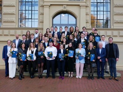 Gruppenfoto der Absolventinnen und Absolventen, die ihre Zeugnismappen und jeweils eine Rose in den Händen halten, der Hochschulleitung und Lehrpersonen, vor dem Hochschulgebäude.