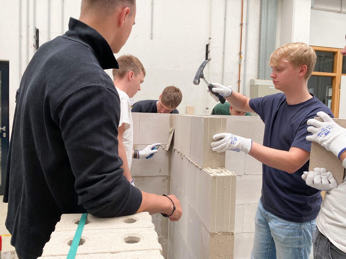 Ein Student klopft mit einem Hammer den Stein des Mauerwerks unter Anleitung eines Experten fest