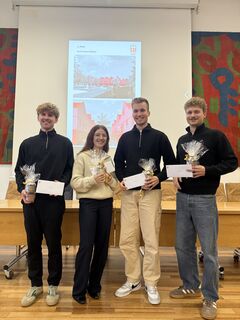 Drei Studenten und eine Studentin mit weißen Briefumschlägen und kleinen Geschenken stehen zusammen.