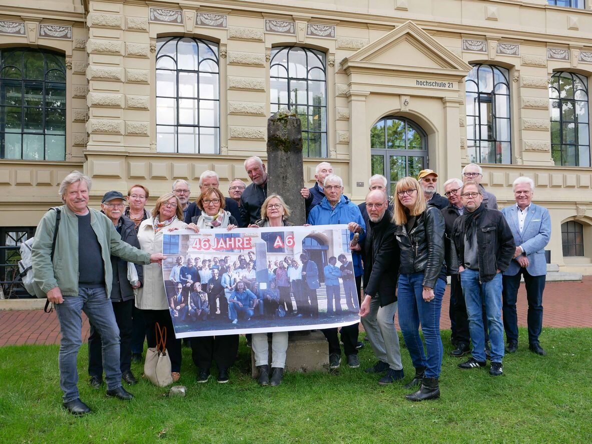 Gruppenfoto der ehemaligen Architekturstudierenden mit ihrem damaligen Professor Eduard Stura und dem jetzigen Hochschulpräsident Prof. Dr.-Ing. Ingo Hadrych mit dem Obelisken vor dem Hochschulgebäude.