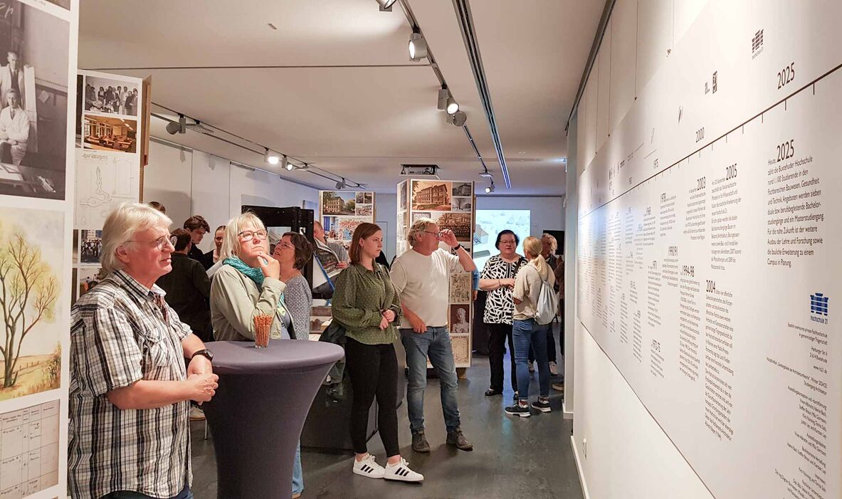 Der Ausstellungsraum mit dem Zeitstrahl rechts an der Wand, der von Besuchern betrachtet wird.